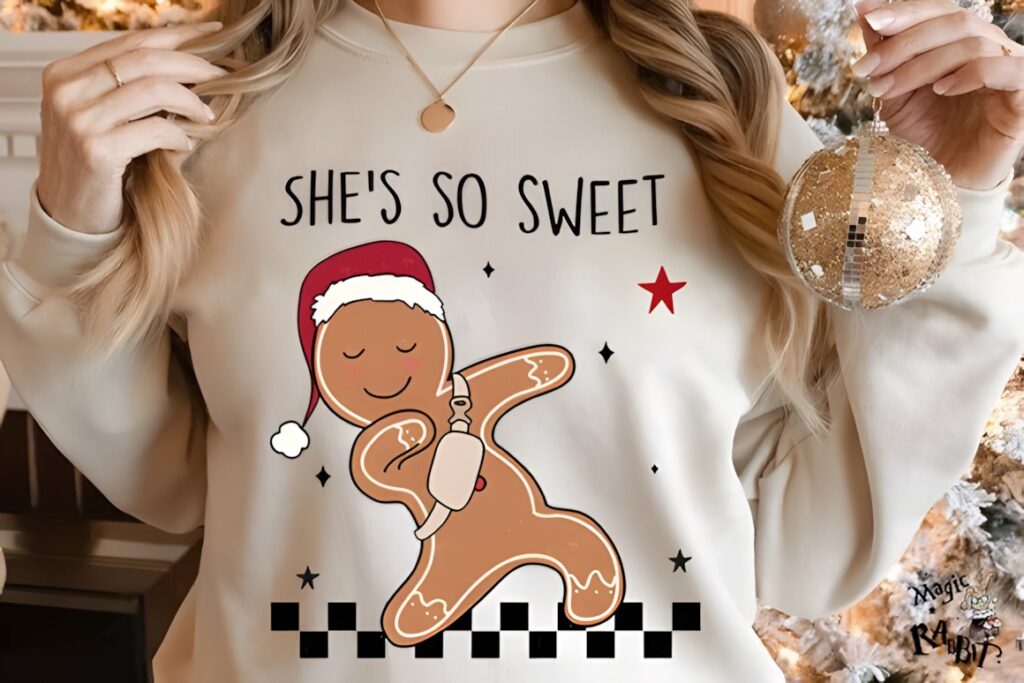 Gingerbread character wearing Santa hat with text she's so sweet on beige sweatshirt Xmas PNG Designs