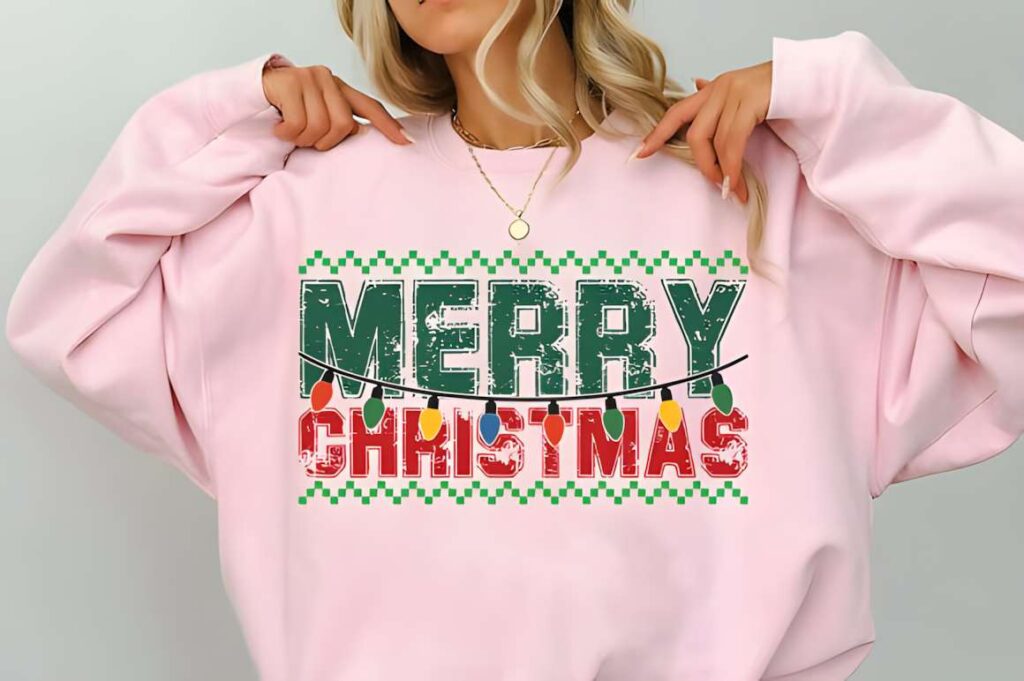 Christmas t-shirt design ideas for POD sellers featuring a pink sweatshirt with a green and red Merry Christmas graphic